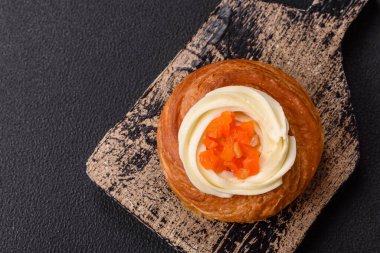 Beyaz krema ve turunçgille kaplı tatlı Danimarka çöreği. Koyu beton bir arka planda krema doluyor.