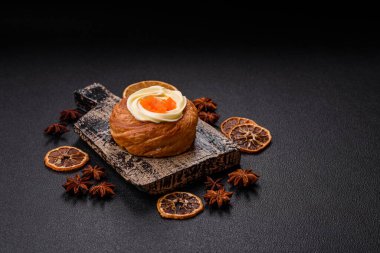 Beyaz krema ve turunçgille kaplı tatlı Danimarka çöreği. Koyu beton bir arka planda krema doluyor.