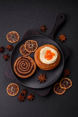 Beyaz krema ve turunçgille kaplı tatlı Danimarka çöreği. Koyu beton bir arka planda krema doluyor.