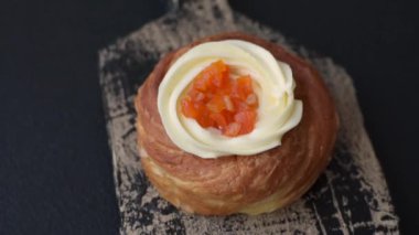 Beyaz krema ve turunçgille kaplı tatlı Danimarka çöreği. Koyu beton bir arka planda krema doluyor.