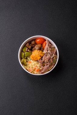 Koyu beton bir zeminde seramik tabakta sebzeli, taneli, tohumlu ve baharatlı haşlanmış biftek.