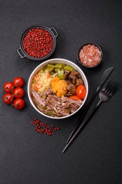 Koyu beton bir zeminde seramik tabakta sebzeli, taneli, tohumlu ve baharatlı haşlanmış biftek.