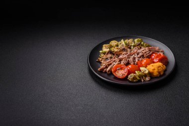 Koyu beton bir zeminde seramik tabakta sebzeli, taneli, tohumlu ve baharatlı haşlanmış biftek.