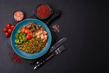 Soya peyniri, buğulanmış sebzeler, tahıllar, tohumlar ve baharatlar ile koyu beton bir arka planda.