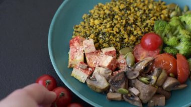 Soya peyniri, buğulanmış sebzeler, tahıllar, tohumlar ve baharatlar ile koyu beton bir arka planda.