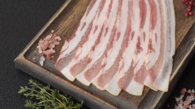 Baharat ve otlarla dilimlenmiş taze çiğ domuz pastırması ve koyu beton bir arka plan.