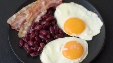 Yağda yumurta, pastırma, fasulye, domates, baharat ve bitkilerle İngiliz kahvaltısı. Güne doyurucu ve doyurucu bir başlangıç.