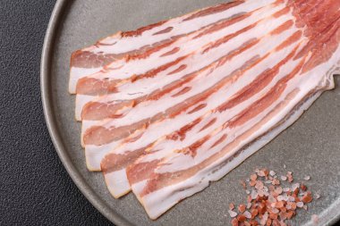 Baharat ve otlarla dilimlenmiş taze çiğ domuz pastırması ve koyu beton bir arka plan.