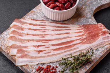 Baharat ve otlarla dilimlenmiş taze çiğ domuz pastırması ve koyu beton bir arka plan.