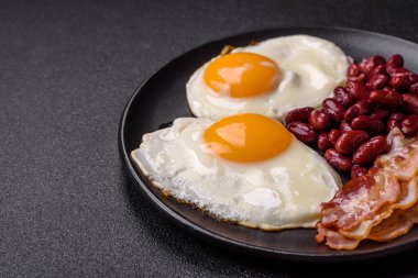 Yağda yumurta, pastırma, fasulye, domates, baharat ve bitkilerle İngiliz kahvaltısı. Güne doyurucu ve doyurucu bir başlangıç.