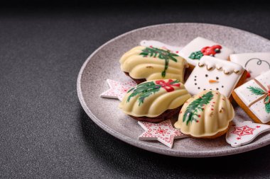 Tatlı Madeleine tatlıları Noel renklerinde çikolatayla kaplıdır. Koyu beton arka planda çeşitli malzemeler vardır.