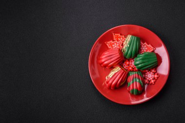 Tatlı Madeleine tatlıları Noel renklerinde çikolatayla kaplıdır. Koyu beton arka planda çeşitli malzemeler vardır.