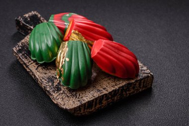 Tatlı Madeleine tatlıları Noel renklerinde çikolatayla kaplıdır. Koyu beton arka planda çeşitli malzemeler vardır.