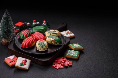 Tatlı Madeleine tatlıları Noel renklerinde çikolatayla kaplıdır. Koyu beton arka planda çeşitli malzemeler vardır.