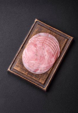 Tuzlu, baharatlı ve otlu füme jambon koyu dokulu arka planda yuvarlak dilimler halinde kesilmiş.