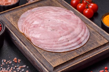 Tuzlu, baharatlı ve otlu füme jambon koyu dokulu arka planda yuvarlak dilimler halinde kesilmiş.