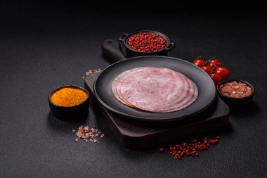 Tuzlu, baharatlı ve otlu füme jambon koyu dokulu arka planda yuvarlak dilimler halinde kesilmiş.