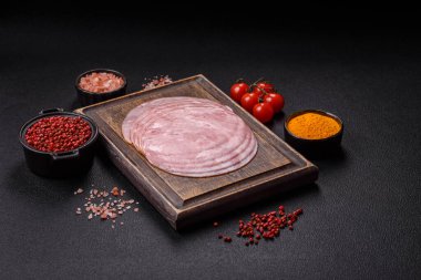 Tuzlu, baharatlı ve otlu füme jambon koyu dokulu arka planda yuvarlak dilimler halinde kesilmiş.