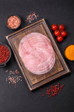 Tuzlu, baharatlı ve otlu füme jambon koyu dokulu arka planda yuvarlak dilimler halinde kesilmiş.
