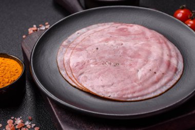 Tuzlu, baharatlı ve otlu füme jambon koyu dokulu arka planda yuvarlak dilimler halinde kesilmiş.