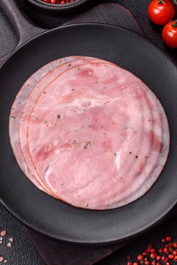 Tuzlu, baharatlı ve otlu füme jambon koyu dokulu arka planda yuvarlak dilimler halinde kesilmiş.