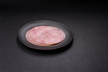 Tuzlu, baharatlı ve otlu füme jambon koyu dokulu arka planda yuvarlak dilimler halinde kesilmiş.