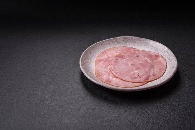 Tuzlu, baharatlı ve otlu füme jambon koyu dokulu arka planda yuvarlak dilimler halinde kesilmiş.