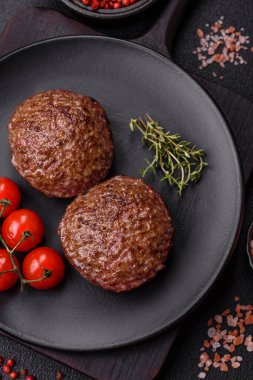 Tuzlu, baharatlı ve otlu sığır burger köfteleri koyu beton arka planda kızartılıyor.