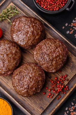 Tuzlu, baharatlı ve otlu sığır burger köfteleri koyu beton arka planda kızartılıyor.