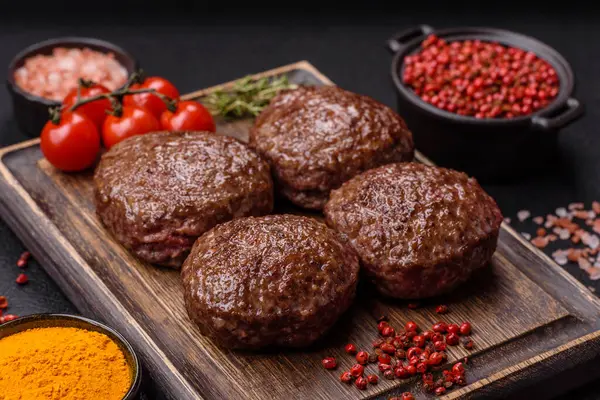 Tuzlu, baharatlı ve otlu sığır burger köfteleri koyu beton arka planda kızartılıyor.