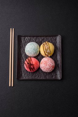 Delicious colorful asian mochi sweets with rice dough shell and fruit filling on dark concrete background clipart