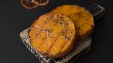 Balkabağı dilimlenmiş, biberiye ve baharatla kızartılmış, koyu beton bir arka planda.