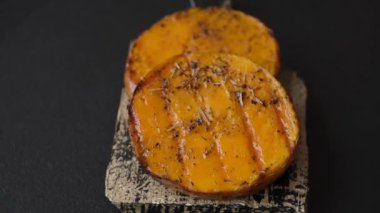 Balkabağı dilimlenmiş, biberiye ve baharatla kızartılmış, koyu beton bir arka planda.