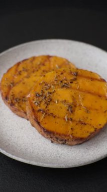 Balkabağı dilimlenmiş, biberiye ve baharatla kızartılmış, koyu beton bir arka planda.