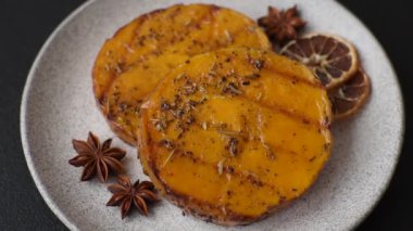 Balkabağı dilimlenmiş, biberiye ve baharatla kızartılmış, koyu beton bir arka planda.