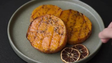 Balkabağı dilimlenmiş, biberiye ve baharatla kızartılmış, koyu beton bir arka planda.