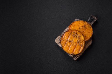 Balkabağı dilimlenmiş, biberiye ve baharatla kızartılmış, koyu beton bir arka planda.