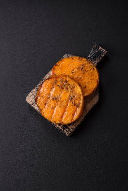 Balkabağı dilimlenmiş, biberiye ve baharatla kızartılmış, koyu beton bir arka planda.