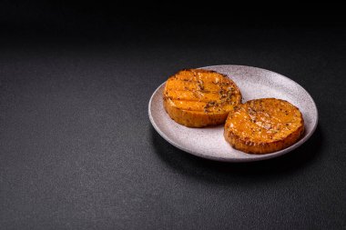 Balkabağı dilimlenmiş, biberiye ve baharatla kızartılmış, koyu beton bir arka planda.