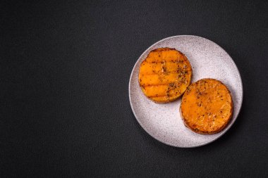 Balkabağı dilimlenmiş, biberiye ve baharatla kızartılmış, koyu beton bir arka planda.