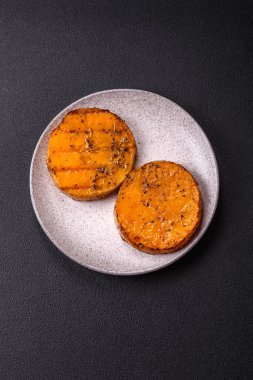 Balkabağı dilimlenmiş, biberiye ve baharatla kızartılmış, koyu beton bir arka planda.