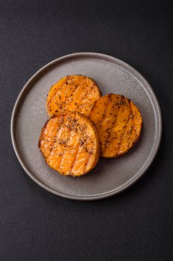 Balkabağı dilimlenmiş, biberiye ve baharatla kızartılmış, koyu beton bir arka planda.