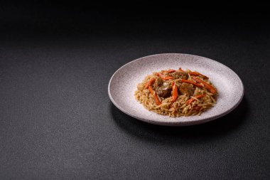 Lezzetli taze pilav, pirinç, havuç, et, soğan, baharat ve böğürtlen ile koyu beton arka planda seramik bir tabakta.