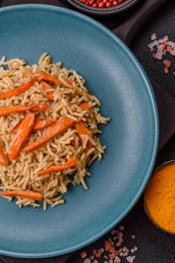 Lezzetli taze pilav, pirinç, havuç, et, soğan, baharat ve böğürtlen ile koyu beton arka planda seramik bir tabakta.