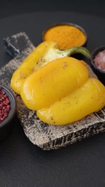 İkiye bölünmüş sarı tatlı biber ve koyu beton arka planda tuz, baharat ve otlarla ızgara.