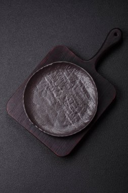 Koyu beton arka planda boş siyah seramik plaka. Aile yemeği için masayı hazırlıyorum.