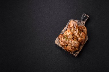 Koyu beton bir arka planda tuzlu, baharatlı ve otlu ızgara kemiksiz tavuk budu.