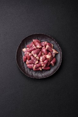 Raw chicken hearts with salt, spices and herbs on a dark concrete background clipart