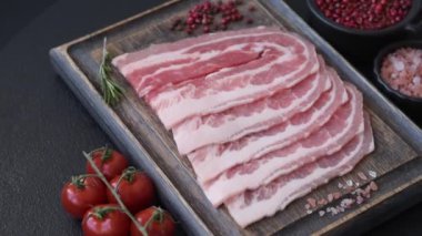 Baharat ve otlarla dilimlenmiş taze çiğ domuz pastırması ve koyu beton bir arka plan.