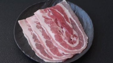 Baharat ve otlarla dilimlenmiş taze çiğ domuz pastırması ve koyu beton bir arka plan.